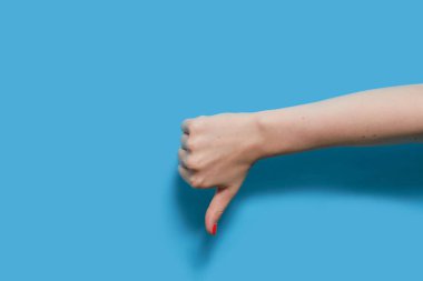 Yapan kadın başparmağını indirerek hoşnutsuzluk işareti gösteriyor. Mavi arka planda kırmızı jel cilası manikürlü bir kadın eli. Boşluğu kopyala