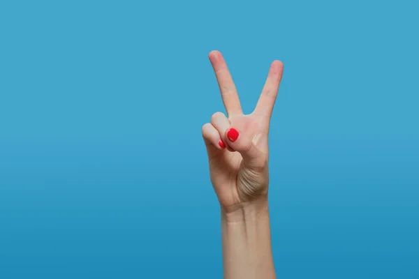 Kadın eli zafer işareti gösteriyor, V harfi mavi arka planda kırmızı jel cilalı kadın eli. Boşluğu kopyala — Stok fotoğraf