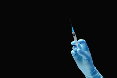Siyah arka planda mavi eldivenli bir doktorun elinde aşı olan şırınga.. 