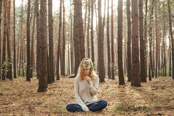 Blanke vrouw zonder gezicht buiten zittend op de grond. Ze bedekte haar gezicht met een sparren tak. Het concept van eenheid met natuur en welzijn. — Stockfoto