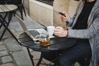 Kafkasyalı yüzü olmayan bir adam sokak kafesindeki bir masaya oturur ve telefona bakar.