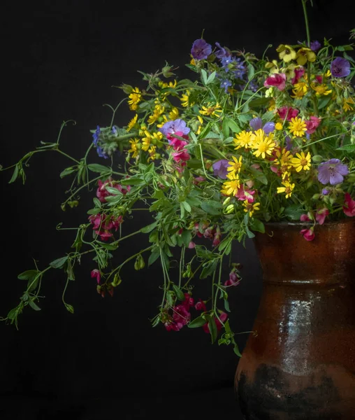 Een ruiker van wilde bloemen in een klei kruik. Stilleven op een zwarte achtergrond. — Stockfoto