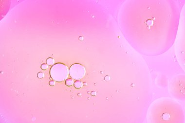 Yatay makro çekim: Pastel renkli bir sıvının içinde yüzen çeşitli boyutlarda şeffaf pembe kabarcıklar grubu. Modern minimalist stil, hafif tonlar, afişler ve tasarım için uygun.