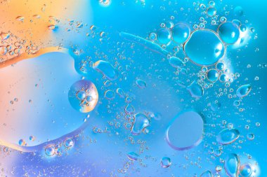 Mavi ve turuncu sıvıda yüzen makro yağ kabarcıkları, şeffaf damlaları, parlak yansımaları ve yumuşak eğimleri olan soyut yapılar. Bokeh efektli yaratıcı, modern doku. 