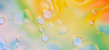 Macro photograph of water droplets against a bright background with smooth transitions of yellow, green, orange, and blue colors. texture is fluid, with bubbles of various sizes, light accents. 