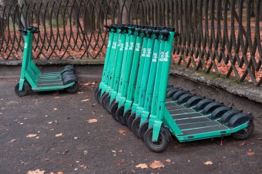 16 Kasım 2025, Ukrayna, Lviv. Elektrikli scooter 'lar karanlık bir sokakta iki sıra halinde dizilmiş. Kaldırımda sonbahar yaprakları, kentsel ortam, geometrik kompozisyon, açık hava aydınlatması. 