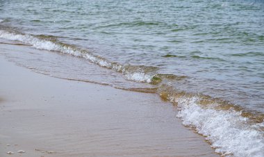 Şeffaf dalgaların kumlu kıyı şeridini kapladığı sakin bir sahne, mikro detaylar ve sakinliğin altını çiziyor. Saflık, yaz için arka plan, rahatlama ya da çevre konuları hakkında konular için harika