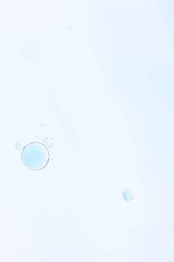 Parlak yumuşak bir zemin üzerinde soluk mavi sıvıyla küçük yarı şeffaf baloncukların dikey makro fotoğrafı, hava dokusuyla minimum soyut kompozisyon ve metin için cömert kopya alanı. 