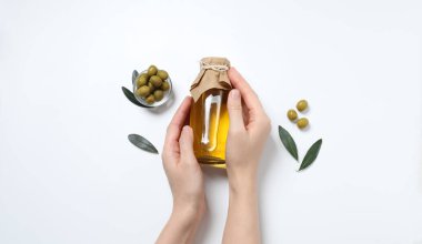 Kadınların elleri beyaz arka planda zeytinli yağ şişesini tutuyor. en üstteki görünüm