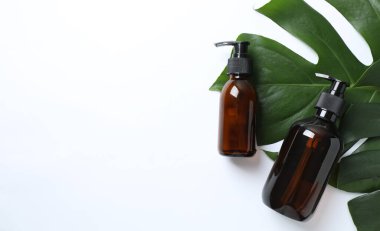 Beyaz zemin üzerinde gerekli yağ şişeleri ve taze tropikal yapraklar