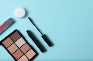 Mavi arka planda güzellik ürünleri. Kozmetik palet, fırça, krem ve ruj. Üst görünüm.