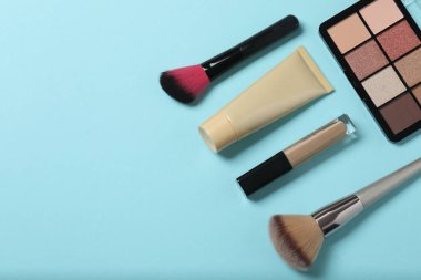 Mavi arka planda güzellik ürünleri. Kozmetik palet, fırça, krem ve ruj. Üst görünüm.