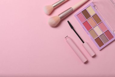 Pembe arka planda kozmetik ürünler. Kozmetik palet, fırçalar, kremler ve rujlar. Üst görünüm.