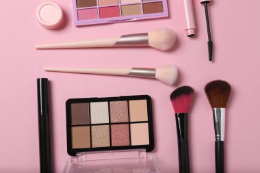 Pembe arka planda kozmetik ürünler. Kozmetik palet, fırçalar, kremler ve rujlar. Üst görünüm.