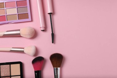 Pembe arka planda kozmetik ürünler. Kozmetik palet, fırçalar, kremler ve rujlar. Üst görünüm.