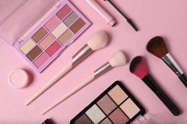 Pembe arka planda kozmetik ürünler. Kozmetik palet, fırçalar, kremler ve rujlar. Üst görünüm.