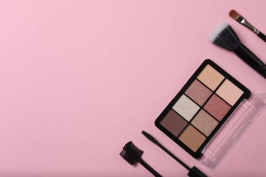 Pembe arka planda kozmetik ürünler. Kozmetik palet, fırçalar, kremler ve rujlar. Üst görünüm.