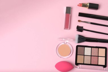 Pembe arka planda kozmetik ürünler. Kozmetik palet, fırçalar, kremler ve rujlar. Üst görünüm.