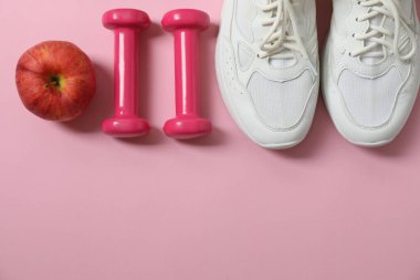 Pullar, spor ayakkabıları, dambıllar ve pembe arka plandaki mezura.