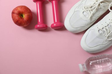 Pullar, spor ayakkabıları, dambıllar ve pembe arka plandaki mezura.