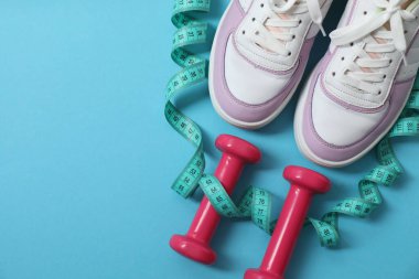 Pullar, spor ayakkabıları, dambıllar ve mavi arka plandaki mezura