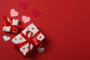 Kırmızı kurdelelere sarılı, kırmızı kalplerle çevrili hediye kutularıyla Sevgililer Günü afişi. Romantik ve şenlikli etkinlikler için ideal.