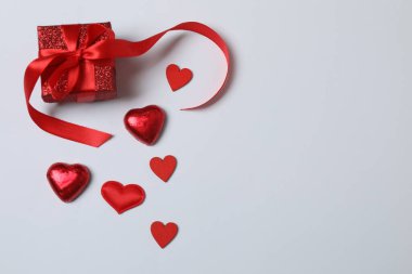 Kırmızı kurdelelere sarılı, beyaz arka planda kırmızı kalplerle çevrili sevgililer günü afişi. Romantik ve şenlikli etkinlikler için ideal.