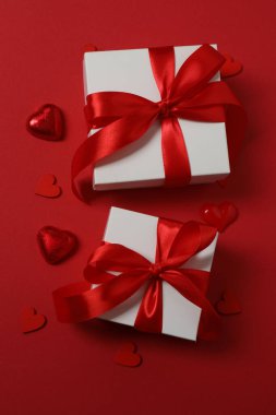 Kırmızı kurdelelere sarılı, kırmızı kalplerle çevrili hediye kutularıyla Sevgililer Günü afişi. Romantik ve şenlikli etkinlikler için ideal.