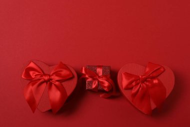 Kırmızı kurdelelere sarılı, kırmızı kalplerle çevrili hediye kutularıyla Sevgililer Günü afişi. Romantik ve şenlikli etkinlikler için ideal.