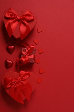 Kırmızı kurdelelere sarılı, kırmızı kalplerle çevrili hediye kutularıyla Sevgililer Günü afişi. Romantik ve şenlikli etkinlikler için ideal.