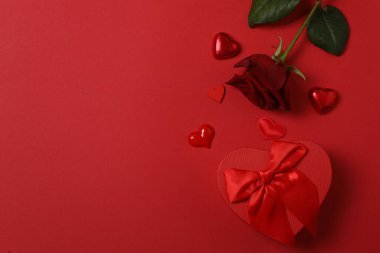 Kırmızı gül, hediye kutusu ve arka plandaki kalpler.