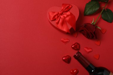 Kırmızı gül, hediye kutusu ve arka plandaki kalpler.