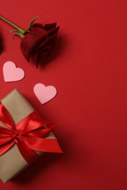 Kırmızı gül, hediye kutusu ve arka plandaki kalpler.