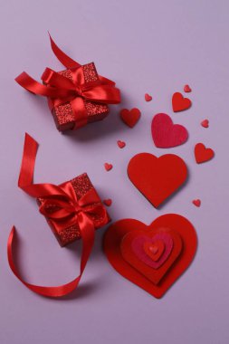 Renkli arka planda kırmızı kalplerle çevrili hediye kutularıyla Sevgililer Günü afişi. Romantik ve şenlikli olaylar için mükemmel..