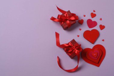 Renkli arka planda kırmızı kalplerle çevrili hediye kutularıyla Sevgililer Günü afişi. Romantik ve şenlikli olaylar için mükemmel..