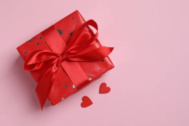 Kırmızı kurdeleli hediye kutusu ve pembe arkaplanlı kurdele.