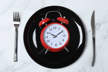 Alarm saati, tabak ve çatal bıçak takımı masada, düz yerde. Diyet rejimi.