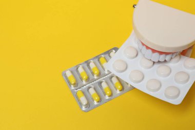 Diş modelinde, sarı arka planda su toplayan ilaç paketleri var.