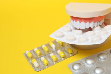Diş modelinde, sarı arka planda su toplayan ilaç paketleri var.