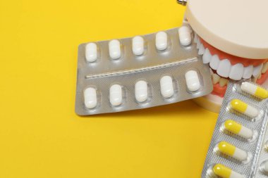 Diş modelinde, sarı arka planda su toplayan ilaç paketleri var.