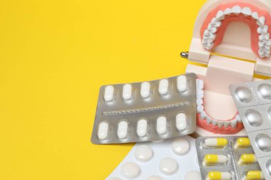 Diş modelinde, sarı arka planda su toplayan ilaç paketleri var.