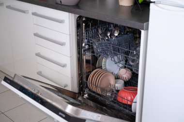 Bulaşık makinesi açık kapılı ve mutfakta bulaşıkları yıkıyor..