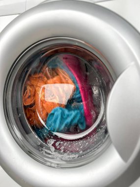 Bir kadının eli çamaşır makinesine çamaşır kapsülü atar..