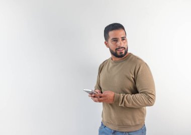 Sıradan süveter giyen yakışıklı bir adam telefon kullanıyor, beyaz bir arka plana bakıyor.