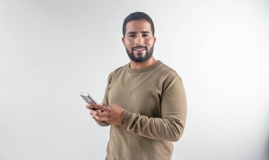 Kahverengi kazaklı mutlu sakallı İspanyol adam temiz beyaz arka planda cep telefonu kullanıyor..