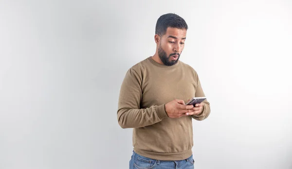 Süveter giyen genç adam cep telefonundan beklenmedik haberler okurken şok olmuş görünüyor.