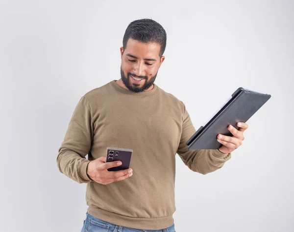 Bir yandan cep telefonu tutarken diğer yandan tablet üzerinde veri danışmanı olan mutlu bir genç adam.