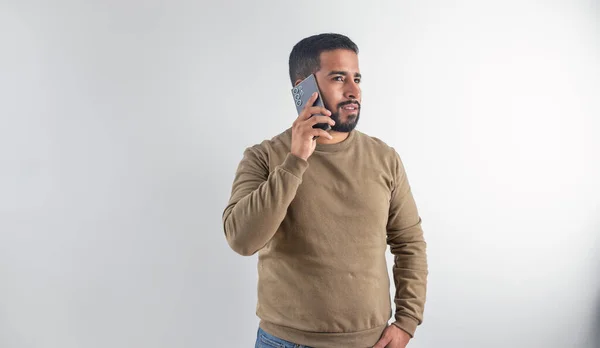 Ciddi bir genç adam cep telefonuyla konuşuyor ve beyaz bir arka plana bakıyor.