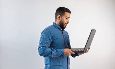 Mavi tişörtlü, elinde dizüstü bilgisayarı olan odaklanmış bir adamın yan profili.