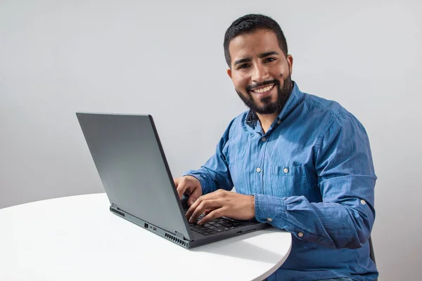 Beyaz bir masada oturmuş, dizüstü bilgisayar kullanarak mutlu mesut oturan neşeli bir iş adamı.